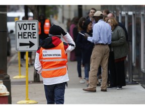 An election official, left, maintains the crowd line and parking spaces as people line up to vote at the Minneapolis Early Vote Center on the last day of early voting Monday, Nov. 5, 2018, in Minneapolis. The Associated Press will debut a new survey of the nation's electorate that aims to more accurately capture the story of how Americans vote and why in Tuesday's midterm elections.