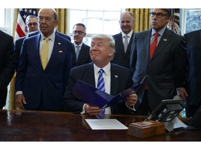 FILE - In this March 24, 2017 file photo, President Donald Trump, flanked by Commerce Secretary Wilbur Ross, left, and Energy Secretary Rick Perry, is seen in the Oval Office of the White House in Washington, during the announcing of the approval of a permit to build the Keystone XL pipeline, clearing the way for the $8 billion project.A federal judge in Montana has blocked construction of the $8 billion Keystone XL Pipeline to allow more time to study the project's potential environmental impact. U.S. District Judge Brian Morris' order on Thursday, Nov. 8, 2018,  came as Calgary-based TransCanada was preparing to build the first stages of the oil pipeline in northern Montana. Environmental groups had sued TransCanada and The U.S. Department of State in federal court in Great Falls.