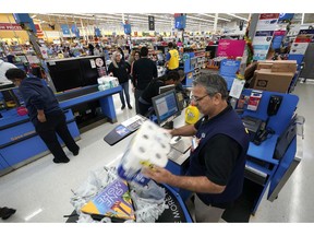 FILE- In this Nov. 9, 2018, file photo Walmart associate Javaid Vohar, right, checks out customers at a Walmart Supercenter in Houston. Walmart Inc. reports earnings Thursday, Nov. 15.