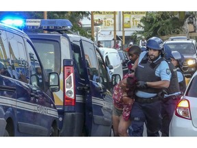 A protester is dragged away and arrested by a police officer after she was seen with others blocking the traffic in Sainte Marie, while protesting against the rising of the fuel and oil prices, in the Indian Ocean island of Reunion, Thursday, Nov. 22, 2018. France is deploying soldiers to stem violence in the Indian Ocean island of Reunion after protests over fuel tax hikes degenerated into looting and rioting.