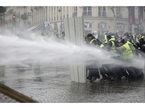 Demonstrators, called the yellow jackets, use a construction barrier to repel a police water canon, during clashes on the famed Champs-Elysees avenue in Paris, France, as they protest against the rising of the fuel taxes, Saturday, Nov. 24, 2018. France is deploying thousands of police to try to contain nationwide protests and road blockades by drivers angry over rising fuel taxes and Emmanuel Macron's presidency.