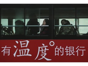 Commuters look out of a window of a bus with a bank advertise during the morning rush hour in Beijing, Tuesday, Nov. 13, 2018. The potential damage to global trade brought on by President Donald Trump's tariffs battle with Beijing is looming as leaders of Southeast Asian nations, China, the U.S. and other regional economies meet in Singapore this week. The advertisement reads "A warm-hearted bank."