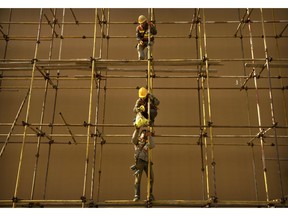 Construction workers pass a bag as they stand on scaffolding outside of a shopping mall in Beijing, Thursday, Nov. 29, 2018. Chinese officials announced last month that the country's quarterly growth rate had slowed to the lowest rate since 2009 as consumer spending and housing sales dampened amid a looming trade war with the United States.