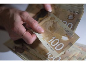 Canadian $100 bills are counted in Toronto, Feb. 2, 2016. A new report warns that as personal debt levels across the country remain near record highs, more Canadian households may find themselves "vulnerable" to interest rate increases. The report says that for every $1 of disposable income, Canadians owe $1.70.