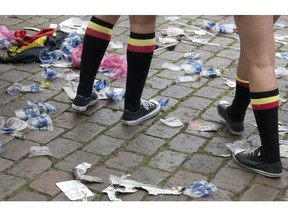FILE - In this June 18, 2016 file photo two Belgian fans, wearing the Belgian colors, walk through plastic cups and other garbage after taking part in a celebration in Antwerp, Belgium, after Belgium won its Euro 2016 Group E match against Ireland. European Union officials have agreed to ban some single-use plastics, such as disposable cutlery, plates and straws, in an effort to cut marine pollution.