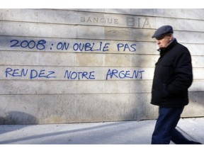 In this photo taken on Thursday, Dec. 13, 2018, a man walks past French graffiti that reads: "2008: We haven't forgotten, Give us back our money", a few blocks from the Champs Elysees in Paris. Across the world, people are questioning truths they had long held to be self-evident, and they are dismissing some of them as fake news. They are replacing traditions they had long seen as immutable with haphazard reinvention. In France, people who feel left behind by a globalizing world have spent the last few weeks marching and rioting to protest a government they call elitist and out of touch.