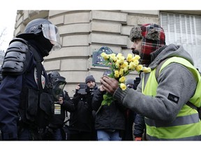 A demonstrator wearing his yellow vest holds a bouquet of roses in front of a riot police officer during a protest Saturday, Dec. 15, 2018 in Paris. Paris police deployed in large numbers Saturday for the fifth straight weekend of demonstrations by the "yellow vest" protesters, with authorities repeating calls for calm after protests on previous weekends turned violent.