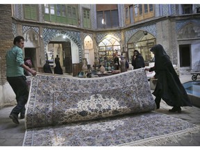 In this Monday, Dec. 10, 2018 photo, two carpet weavers open their hand-woven carpet at the grand bazaar in Kashan, Iran. Before the Trump administration withdrew from Iran's nuclear deal with word powers and began restoring crippling sanctions earlier this year, the $425 million a year Persian carpet industry kept an ancient artistic tradition alive while providing much-needed income to Iranians as well as Afghan refugees, who create much of the more luxurious hand-woven pieces.
