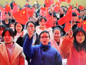 This photo taken on December 18, 2018 shows students waving flags at Huaibei Normal University in Huaibei in China's eastern Anhui province as they watch live coverage of a speech in Beijing by China's President Xi Jinping to mark the 40th anniversary of China's reform and opening policy.