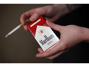 FILE - In this July 17, 2015, file photo, store manager Stephanie Hunt poses for photos with a pack of Marlboro cigarettes, an Altria brand, at a Smoker Friendly shop in Pittsburgh.  Altria is diving into the Canadian cannabis market with a $2.4 billion investment in Toronto-based medical and recreational marijuana provider Cronos Group. The investment from Altria Group Inc.,  would give it about 45 percent ownership of Cronos. Altria will also pay another $1.4 billion for warrants of Cronos Group that if exercised, would give the Altria a 55 percent majority ownership of Cronos.