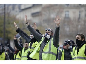Masked demonstrators wearing yellow jackets raise their hands near the Champs-Elysees avenue during a demonstration Saturday, Dec.1, 2018 in Paris. Scuffles broke out between some French protesters angry over rising taxes and police for a third straight weekend, after small pockets of demonstrators built barricades in the middle of streets in central Paris and lit fires Saturday.