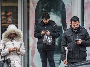 Three pedestrians looking at smartphones in Toronto.