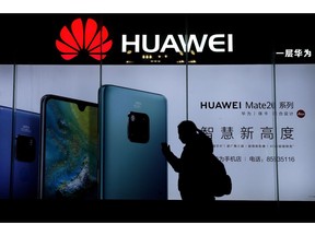 A woman browses her smartphone as she walks by a Huawei store at a shopping mall in Beijing, Tuesday, Dec. 11, 2018. China's foreign minister vowed Tuesday to protect its citizens abroad as a Canadian court decided whether to release a technology executive on bail in a case that has riled U.S.-Chinese relations.