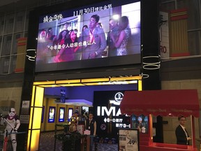In this Tuesday, Dec. 4, 2018, photo, a worker stands underneath a screen advertising the movie "Crazy Rich Asians" at a cinema in Beijing. Chinese audiences aren't exactly going nuts over the U.S. box office hit "Crazy Rich Asians," despite its all-Asian cast and theme of rising Asian prosperity.