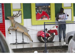 A man reads a newspaper next to Santa Claus on a cart in Harare, in this Sunday, Dec. 9 , 2018 photo.  The Holiday mood is not catching on in Zimbabwe where a currency crisis has forced people to risk jail time to buy basics such as medicine and food, often tapping the black market with daily transactions dominated by the U.S. dollar.