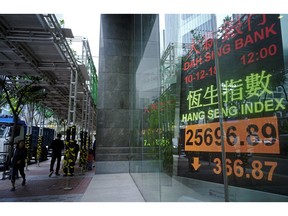 People walk past an electronic board showing Hong Kong share index outside a local bank in Hong Kong, Monday, Dec. 10, 2018. Asian markets were broadly lower Monday after China protested the arrest of a senior executive of Chinese electronics giant Huawei, who is suspected of trying to evade U.S. trade curbs on Iran.