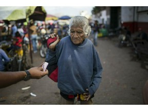 An elderly woman is offered cash as she begs at a wholesale food market in Caracas, Venezuela, Monday, Jan. 28, 2019. Economists agree that the longer the standoff between the U.S.-backed opposition leader Juan Guaido and President Nicolas Maduro drags on, the more regular Venezuelans are likely to suffer.