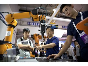 FILE - In this Aug. 18, 2018, file photo, visitors look at a manufacturing robot from Chinese robot maker Aubo Robotics at the World Robot Conference in Beijing, China. China's government has appealed to Washington to accept its industrial progress after U.S. intelligence officials said Beijing helps to steal and copy foreign technologies.