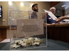 A donation box sits on the counter as Dany Garcia speaks with visitors at the Ernest F. Coe Visitor Center in Everglades National Park, Friday, Jan. 4, 2019, in Homestead, Fla. Garcia is being paid by the Florida National Parks Association to work in the center during the partial government shutdown. As the shutdown drags on, private organizations, local businesses, volunteers and state governments are putting up the money and manpower to keep national parks across the U.S. open, safe and clean for visitors.