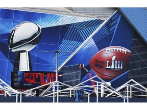 In this  Jan. 17, 2019 photo,  workers use a lift to install a Super Bowl 53 wrap on the outside of Mercedes-Benz Stadium as it is transformed for the big NFL football game in Atlanta.   Kraft Heinz' frozen-food brand Devour is trying to make waves during its Super Bowl debut with an ad taking a humorous jab at one man's "frozen food porn addiction." Super Bowl ads have long used raunchiness and sex stand out during the Super Bowl, advertising's biggest stage. But the approach runs the risk of offending the audience.