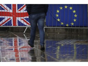 Flags tied to railings outside parliament are reflected on a wet pavement in London, Thursday, Jan. 24, 2019. The European Union's chief Brexit negotiator, Michel Barnier, is rejecting the possibility of putting a time limit on the "backstop" option for the Irish border, saying it would defeat the purpose.