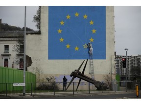 A man takes a photograph of a mural by street artist Banksy, depicting a star being chiselled from the European flag in Dover, south-east England, Monday, Jan. 7, 2019. Britain is testing how its motorway and ferry system would handle a no-deal Brexit split from the European Union by sending a stream of trucks from a regional airport to the port of Dover.