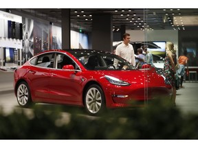 FILE- In this July 6, 2018, file photo, a prospective customer confer with sales associate as a Model 3 sits on display in a Tesla showroom in the Cherry Creek Mall in Denver. On Tuesday, Jan. 1, 2019, the federal credit for Tesla buyers dropped from $7,500 to $3,750. It will gradually be phased out this year.