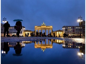 People walks in front of the Brandenburg Gate that is reflected in a puddle in Berlin, Germany, on a rainy Sunday, Jan. 13, 2019.