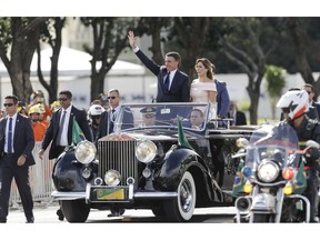 Flanked by first lady Michelle Bolsonaro, Brazil's President Jair Bolsonaro waves as he rides in an open car after his swearing-in ceremony, in Brasilia, Brazil, Tuesday, Jan. 1, 2019.