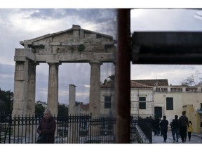 People are seen through the netting of a scaffolding as they walk in front of the Gate of the ancient Roman agora in Plaka district of Athens on Wednesday, Jan. 23, 2019.