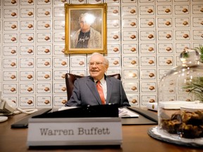 Warren Buffett sits behind a desk under a portrait of founder Mary See at the See's Candies booth during part of the 2016 Berkshire Hathaway AGM.
