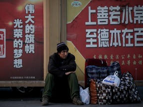 A migrant worker sits next to his belongings against a wall displaying a Chinese government propaganda message at the Beijing railway station in Beijing, Monday. China's economic growth hit a three-decade low in 2018.