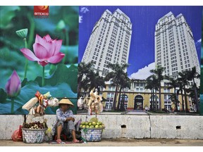 FILE - In this April 29, 2015, file photo, a snack and fruit vendor waits for customers near the advertisement board of a shopping mall and apartment building in Ho Chi Minh City, Vietnam. Vietnam, the location of U.S. President Donald Trump's next meeting with North Korean leader Kim Jong Un, has come a long way since the U.S. abandoned its war against communist North Vietnam in the 1970s.