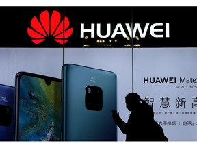 FILE - In this Dec. 11, 2018, file photo, a woman browses her smartphone as she walks by a Huawei store at a shopping mall in Beijing. China's government has accused Washington of trying to block its industrial development after Vice President Mike Pence said Chinese tech giant Huawei and other telecom equipment suppliers are a security threat.