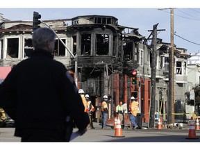 A San Francisco Police officer watches as a crew works at the scene of a Wednesday fire on Geary Boulevard in San Francisco, Thursday, Feb. 7, 2019. A gas explosion in shot a tower of flames into the sky and burned five buildings including one of the city's popular restaurants before firefighters brought the blaze under control.