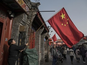 A Chinese woman hangs a national flag outside her business.