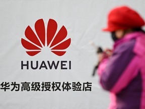 A woman using her smartphone while walking past advertising outside a Huawei store in Beijing.