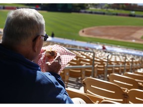 FILE - In this March 4, 2015 file photo, a fan eats a hot dog before a spring training exhibition baseball game between the Chicago White Sox and the Los Angeles Dodgers, in Phoenix. Owners who take customers to sporting events or the theater or treat them to a round of golf will have to foot the entire bill for those activities. The new tax law has done away with the entertainment deduction for businesses.