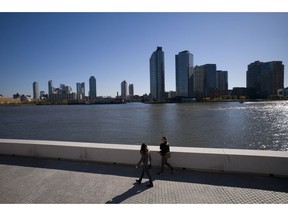 FILE- In this Nov. 7, 2018, file photo a couple walks along Four Freedoms State Park on Roosevelt Island in the Queens borough of New York. Beyond is the Long Island City skyline. According to experts analyzing the e-commerce giant's sudden cancellation of plans to build a massive headquarters in New York City, Amazon's decision to walk away could scare off other tech companies considering moving to or expanding in the city.
