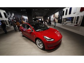 FILE - In this Feb. 9, 2019, file photograph, buyers look over a Model 3 in a Tesla store in Cherry Creek Mall in Denver. Tesla is shifting all of its sales from stores to the internet, saying the move is needed to cut costs so it can sell the mass-market Model 3 for a starting price of $35,000. The Palo Alto, California, company announced the change Thursday, Feb. 28.