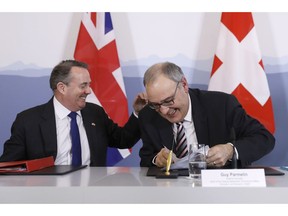 Swiss Federal Councillor Guy Parmelin, right, and British Secretary of State for International Trade Liam Fox, left, react after signing a trade agreement in Bern, Switzerland, Monday, Feb. 11, 2019. Parmelin and Fox signed a bilateral trade agreement regulating relations between the two countries after the Brexit. Because of the customs treaty with Switzerland, the agreement also applies to Liechtenstein.