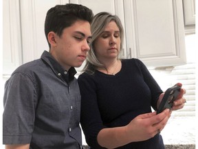 FILE- In this Jan. 31, 2019, file photo Grant Thompson and his mother, Michele, look at an iPhone in the family's kitchen in Tucson, Ariz., on Thursday, Jan. 31, 2019. Apple has released an iPhone update to fix a FaceTime flaw that allowed people to eavesdrop on others while using its group video chat feature. The repair is included in the latest version of Apple's iOS 12 system, which became available to install Thursday. Apple credited the Tucson teenager, Grant Thompson, for discovering the FaceTime bug.