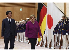 German Chancellor Angela Merkel, center, and Japanese Prime Minister Shinzo Abe, left, review honor guards ahead of a meeting at Abe's official residence in Tokyo Monday, Feb. 4, 2019.