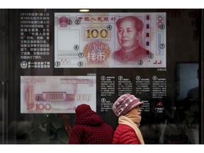 Women walk by a bank window panel displaying the security markers on the latest 100 Yuan notes in Beijing, Monday, Feb. 18, 2019. China's policy ministry says it investigated 380 online lenders and froze $1.5 billion in assets in a crackdown following an avalanche of scandals in the huge but lightly regulated industry.