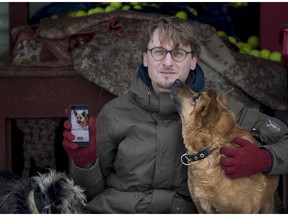 In this photo taken on Saturday, Feb. 2, 2019, Vaidas Gecevicius, who developed an app helping to match stray dogs with potential owners, poses for a picture with a dog and shows this dog's profile on the app in Vilnius, Lithuania.  A group of enthusiasts have launched an app that helps match aspiring dog owners with stray dogs.