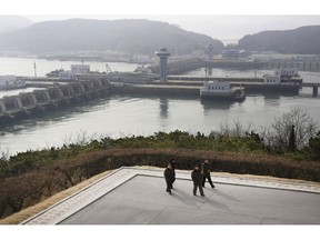 In this Feb. 2, 2019, photo, North Koreans men walk with the background of the West Sea Barrage in Nampo, North Korea. North Korea is exploring two ambitious alternative energy sources, tidal power and the production of coal-based synthetic fuels, that could greatly improve its standard of living while reducing its reliance on oil imports and vulnerability to sanctions.