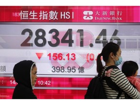 People walk past an electronic board showing Hong Kong share index outside a bank in Hong Kong, Thursday, Feb. 14, 2019. Asian stocks were mostly lower on Thursday as China and the U.S. kicked off two days of trade negotiations in Beijing.