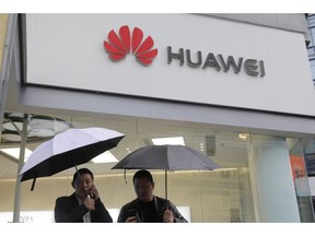 FILE - In this Thursday, March 7, 2019 file photo, two men use their mobile phones outside a Huawei retail shop in Shenzhen, China's Guangdong province. British cybersecurity inspectors have found significant technical issues in Chinese telecom supplier Huawei's software that they say pose new risks for the country's telecom companies. The annual report Thursday, March 28, 2019 said that because of Huawei's involvement in Britain's critical telecom networks it can only give "limited assurance" that long-term national security risks can be adequately managed.