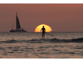 In this Dec. 31, 2013, file photo, a paddleboarder looks our over the Pacific Ocean as the sun sets off of Waikiki Beach, in Honolulu.