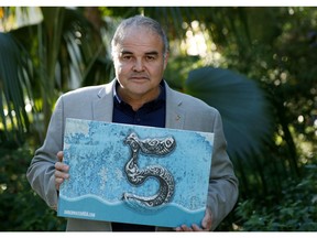 In this Wednesday, Feb. 6, 2019 photo, artist Xavier Cortada poses with a yard sign stating that the area is five feet above sea level in Pinecrest, Fla. Cortada created an "Underwater Homeowner's Association," a kind of community installation to promote awareness about rising sea levels. Participating homeowners get signs in their yards noting how many feet about sea level they stand, and they are holding real meetings, like any other homeowner's association, to discuss how their suburban community can prepare for the effects of climate change.